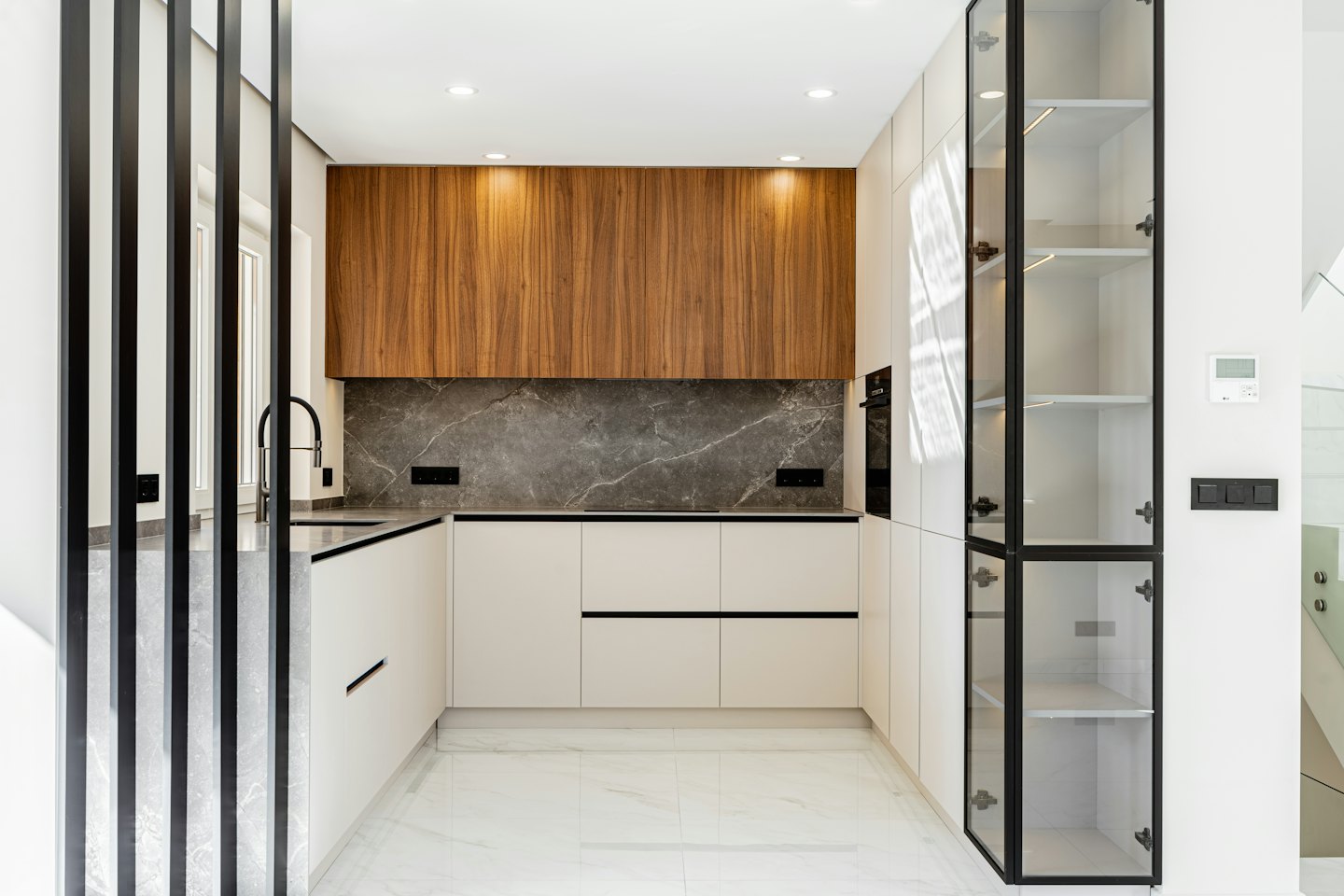 Cucina moderna a U con pensili inferiori color crema e pensili superiori in legno.