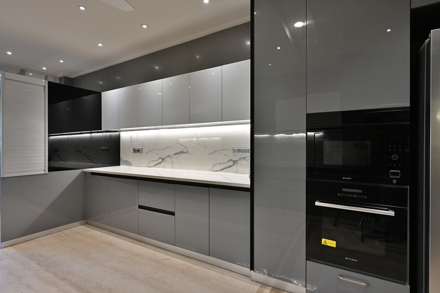 Cucina moderna grigia con paraschizzi in marmo bianco ed elettrodomestici neri.